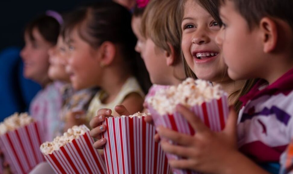 Children sit together at the Kids’ Club Movie Night, enjoying popcorn and watching a family-friendly film in a cozy, fun-filled setting.